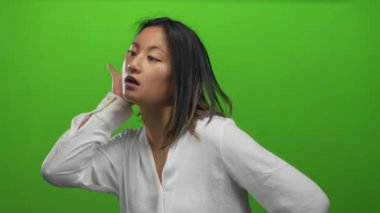 Beyaz tişörtlü genç Çinli kadın yeşil arka plana karşı dinleme hareketi yapıyor.