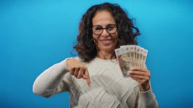 Elinde mavi arka planda Rus rublesi tutan gülümseyen bir kadın orta yaş yaşam tarzında finans, zenginlik ve para odaklarını gösteriyor..