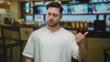 Sakallı genç adam, bir restoranın barında modern iç tasarım ve günlük atmosfer sergileyerek mizahi bir şekilde işaret ediyor..