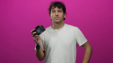 İspanyol adamın elinde kamera, canlı pembe arka plana karşı duruyor. Fotoğraf yeteneklerini sanatsal bir yetenek ve çekici bir görsel varlıkla gösteriyor..