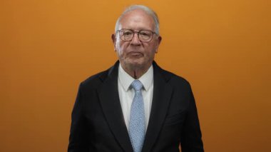 Takım elbiseli kıdemli bir adam canlı turuncu arka planda liderlik ve deneyime karşı güven içinde hareket ediyor..