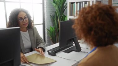 Kadınlar, modern işyerindeki ofis masasında bilgisayarlarla iş belgelerini tartışıyor.