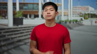 Bir sokak ortasında şehir merkezinde duran genç Çinli bir adam. Bir eli göğsünde, diğeri ise modern mimarinin önünde yükselen kırmızı bir gömlek giyiyor..
