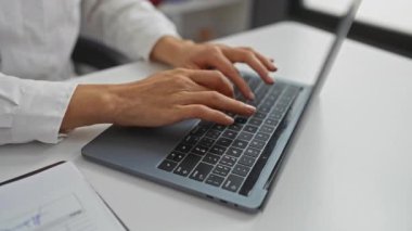 Hastane odasında dizüstü bilgisayarda yazan bir kadın, elleri klavyede ve steteskopta görünür bir şekilde duran, profesyonel sağlık hizmeti veren bir kadın..