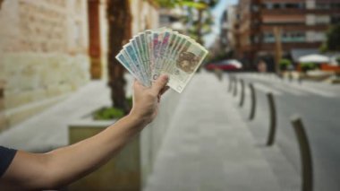 Şehrin bir caddesinde dikilirken elinde Polonyalı zloti banknotları tutan adam bulanık binaları ve kaldırımları olan şehir dışı bir arka planda para sergiliyor..