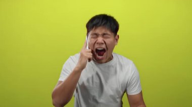 Genç Çinli adam telefonda izole edilmiş sarı duvar arkasına karşı konuşuyor. Güçlü duygular sergiliyor..