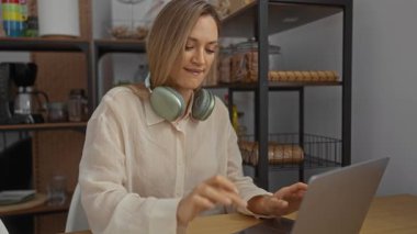 Ofis ortamında gülümseyen kadın kulaklık takıyor, bilgisayarını kapattıktan sonra müzik dinliyor, modern raflar ve şık dekorlarla çevrili, rahat bir çalışma ortamı sergiliyor..