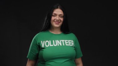 Yeşil tişörtlü gönüllü bir kadın, siyah arka planda pozitiflik ve toplum ruhunu dışa vuruyor.