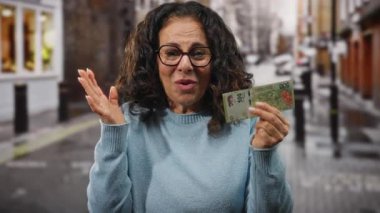 Bir şehir caddesinde elinde Arjantin banknotlarıyla gülümseyen bir kadın mutluluğu ve açık havada mali şansı ifade ediyor gözlük ve süveter takarak heyecanını gösteriyor..