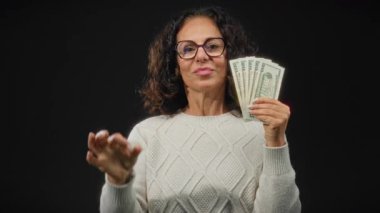 Gözlüklü orta yaşlı bir kadın siyah bir geçmişe karşı iyi bir jest yaparak Amerikan doları tutuyor. Bu da güven ve finansal başarıyı gösteriyor..