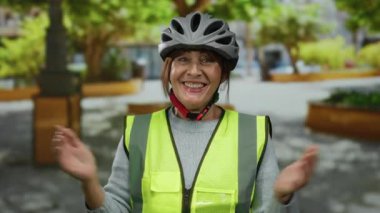 Parkta parlak bir yelek ve miğfer takmış, sıcacık bir gülümsemeyle, açık hava egzersizinin tadını çıkaran, neşeli İspanyol bir kadın..