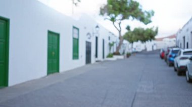 Ianzarote 'de odanmamış sokak manzarası, kanarya adalarındaki sessiz, açık bir sokakta yeşil kapıları ve park etmiş arabaları olan beyaz binaları gösteriyor..