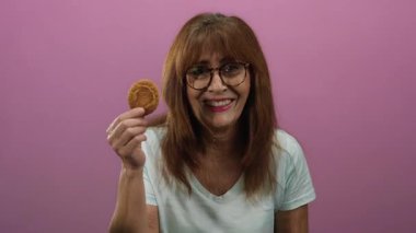 İspanyol kadın elinde kurabiyeyle pembe arka planda gülümsüyor. Mutluluk ve keyif gösteriyor..