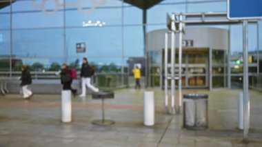 Bulanık figürler cam cephe ile açık hava havaalanı terminalinde geziniyor, kentsel ışık altında yapılan seyahatin hızını yakalıyor.