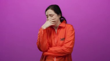 Turuncu hapishane tulumlu, esmer saçlı bir kadın canlı pembe bir arkaplandan endişeli görünüyor. Hassasiyet ve duygusallık hissi veriyor..