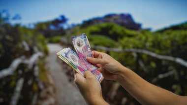 Bir şehir parkında Hong Kong Doları banknotları tutan adam şehir ortamında finans, yatırım ve döviz kurunu sembolize ediyor.