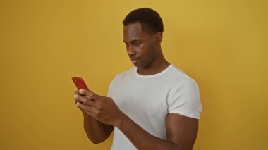 Genç adam, sarı arka planda, modern gündelik kıyafetlerde akıllı telefon tutuyor. Gelişigüzel bir teknoloji kullanıyor, yakışıklı ve çekici özellikleri vurguluyor..