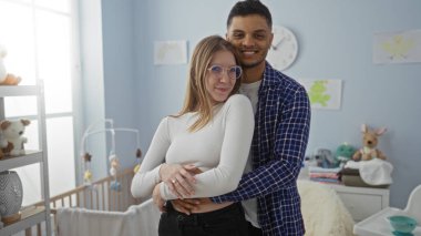 Sıcak bir yatak odasında gülümseyen ve kucaklaşan bir çift. Beşik ve yumuşak bir dekor, aşk, birliktelik ve sıcak bir ev ortamında beklenti..