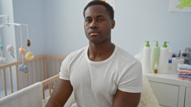 Yatak odasında beşikte oturan genç bir adam, sakin bir yüz ifadesi sergiliyor rahat ve hafif bir iç dekorda..