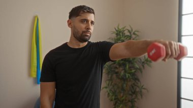 Spor salonunda halterlerle egzersiz yapan, spor salonuna odaklanmış, siyah gömlek giyen, iyi ışıklandırılmış spor merkezinde spor yapan genç bir İspanyol..