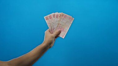 Elinde Türk lira banknotları tutan adam mavi arka plan duvarına izole edilmiş, finansal konsept ve para yönetimini minimalist bir ortamda resmediyor..