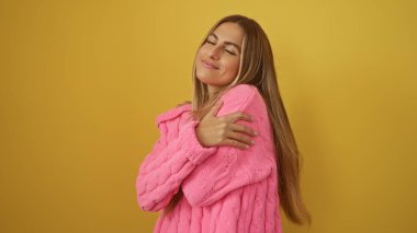 Sarı duvarın üzerinde pembe kazak giyen, kendine güvenen, kendine güvenen ve tarzını sergileyen bir kadın..