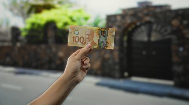 Şehir caddesinde elinde Kanada doları banknotu tutan adam, kentsel finans temaları ve açık hava ticaret faaliyetlerini ön plana çıkarıyor.