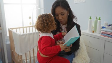 Yatak odasında kızına kitap okuyan bir kadın. Etrafı bebek eşyalarıyla çevrili. Aile sevgisini gözler önüne seriyor..