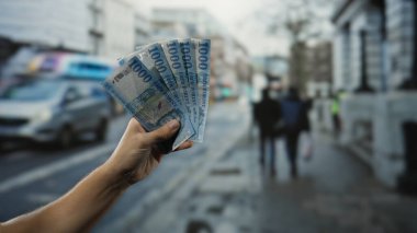 Macar banknotları elinde tutan adam hareketli bir şehir caddesinde kentsel titreşimlerle bağlantılı finansal bir konsept yaratıyor..