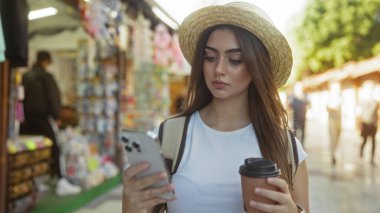 Şehir pazarında elinde kahve tutan şapkalı, akıllı bir kadın. Geçmişi bulanık. Gündüzleri yoğun bir sokak aktivitesi olduğunu gösteriyor..