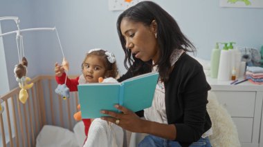Bebek beşikte oynarken, kız kıza kitap okuyan bir kadın, aile sevgisini yakalıyor ve samimi bir evde bağ kuruyor..