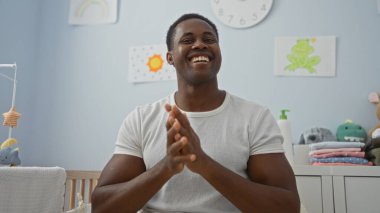 Bebek beşiği ve renkli dekoruyla rahat bir yatak odasında keyifle alkışlayan yakışıklı bir adam ev dekorunda mutluluk ve sıcaklık taşıyor..