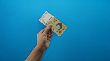 Güney Kore 'yi elinde tutan adamın eli, mali konsepti gösteren izole edilmiş mavi arka plan duvarının üzerinde banknot kazandı..