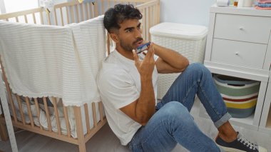 Sakallı genç adam yatak odasının içinde beşikte otururken telefonla sesli mesaj yolluyor..