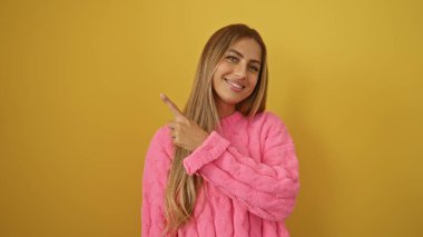 Sarı arka planda izole edilmiş pembe kazak giyen gülümseyen kadın mutluluk ve pozitifliği gösteriyor.