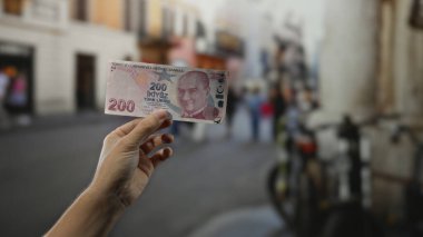 Şehir caddesinde Türk lira banknotu tutan adam güneşli bir günde parlak şehir yaşamını bulanık arka plan ve bisikletlerle yakalıyor..