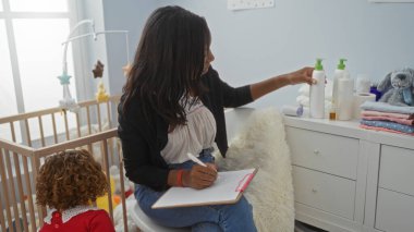Yatak odasında oturan bir kadın, yanında beşiği olan bir çocukla deftere bir şeyler yazıyor ve şifoniyerin üzerine bebek bakımı yapan bir aile ortamı öneriyor..