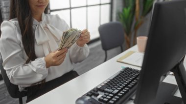 Ofiste iş yerinde para sayan bir kadın bluz giyiyor bilgisayarın yanına bakıyor ve kağıt işleriyle uğraşıyor.