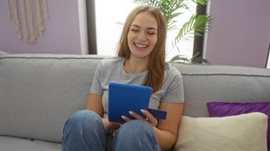 Bir kadın, elinde kredi kartıyla bir dairede kanepeye uzanmış tablet kullanırken rahat bir evde gülümseyen bir kadınla samimi bir anı yakalıyor..