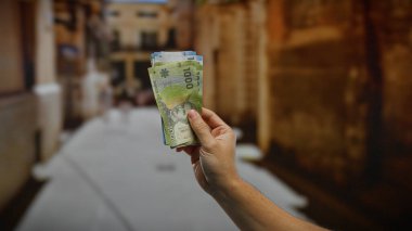 Bir şehir caddesinde Şili pezosu tutan adam, yatırımı ve açık havayı sembolize ediyor, şehir yaşamını ve açık havada ekonomik aktiviteleri yakalıyor..