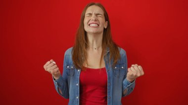 Kırmızı arka planda izole edilmiş kutlayan bir kadın heyecanlı bir ifade ve havada neşeli yumruklarla.