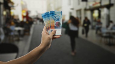 Kalabalık bir şehir caddesinde elinde İsviçre frangı banknotları tutan adam, açık hava ortamında ticaret ve ticaretin özünü yakalıyor..