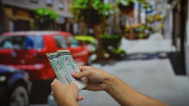 Şehir caddesinde park etmiş arabalarla Malezya halkaları tutan adam, mali işlemleri veya şehir dışında kira ödemelerini vurguluyor.