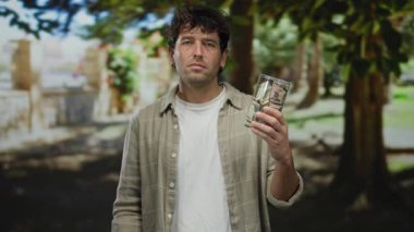 Parkta dolarlar tutan İspanyol bir adam ve duraklama hareketi yapıyor. Çevresi yemyeşil, huzurlu bir açık hava ortamında..