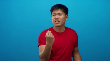 Kırmızı tişörtlü, mavi arka planda kafası karışmış genç bir adam.