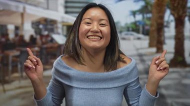 Canlı bir şehir terasında gülümseyen ve farklı yönlere bakan bir kadın şehir ortamında canlı bir sokak atmosferini yakalıyor..