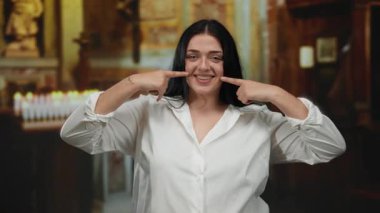 Kilisenin içinde gülümseyen bir kadın, arka planda mumlarla yanaklarını göstererek sakin bir atmosfer yaratıyor..