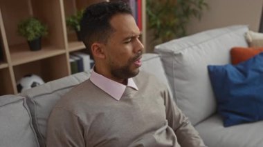 Evin içinde boğazını tutan bir adam sıcak bir apartman dairesinde bitkilerle ve yastıklarla rahatsız görünüyor. Soğuk mevsimde ya da alerjide rahatsızlık olduğunu gösteriyor..