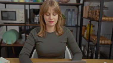 Kadın dizüstü bilgisayarı kapatıyor ve açık bir ofiste raflar, şişeler ve görünür bir mikrodalga fırınla gülümsüyor..