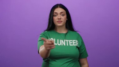Bir jest yapan kadın, mor bir arka planı işaret ederek yeşil bir gönüllü gömleği giyip, kendine güvenini ve kendine güvenini ifade ederek oradan ayrılmak istiyor..